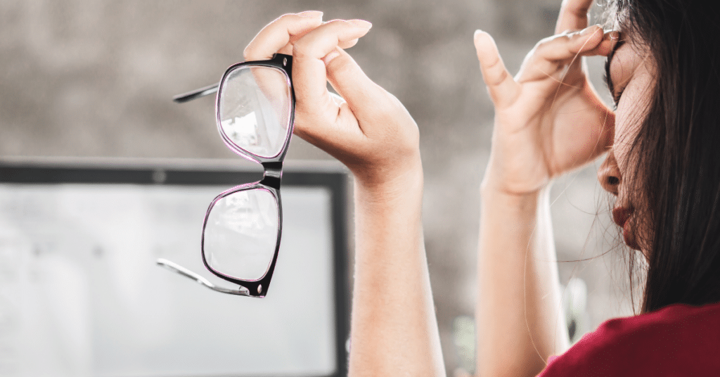 Woman holding eyeglasses experiencing discomfort