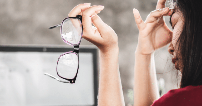 Woman holding eyeglasses experiencing discomfort